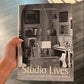 Book titled 'Studio Lives' by Louise Campbell held by a hand on a reflective surface.