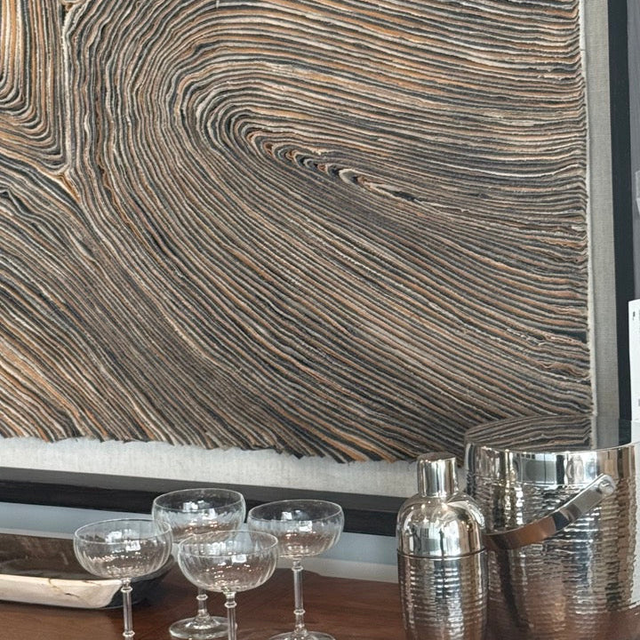 Wooden bar counter with cocktail glasses and shaker against a textured wall.