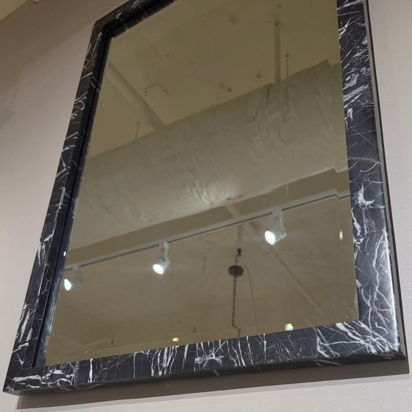 Rectangular mirror with a black marble-like frame on a wall.
