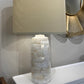 Table lamp with a textured base and beige shade on a surface.