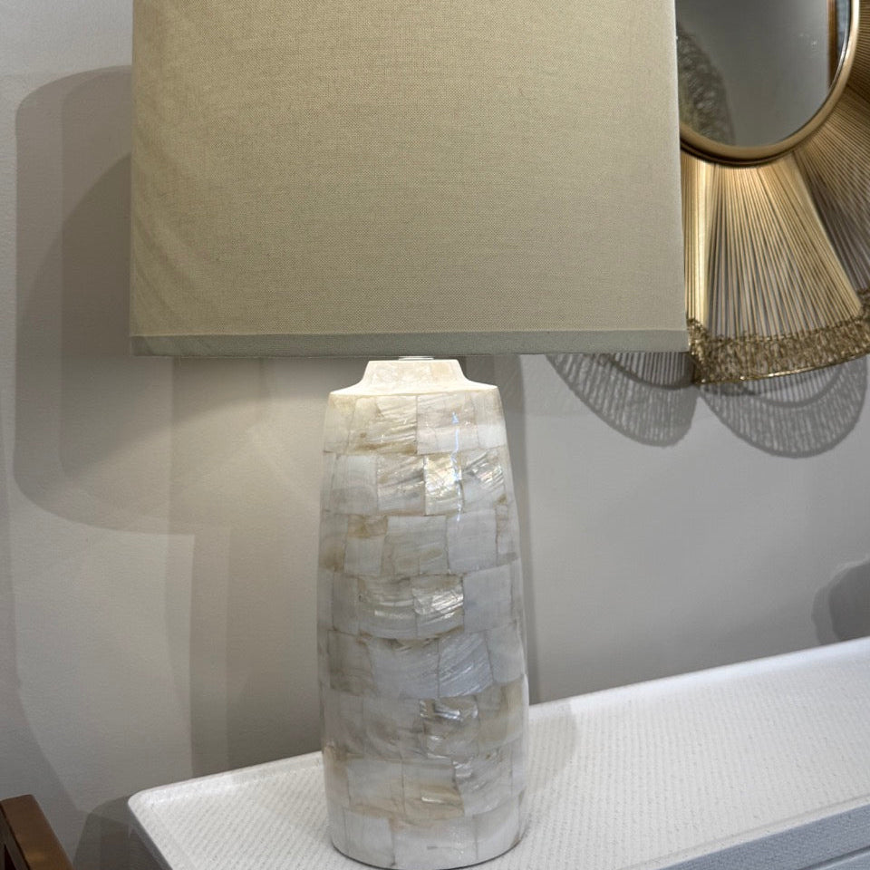 Table lamp with a textured base and beige shade on a surface.