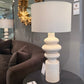 Decorative lamp with a textured base on a round table in a room setting.