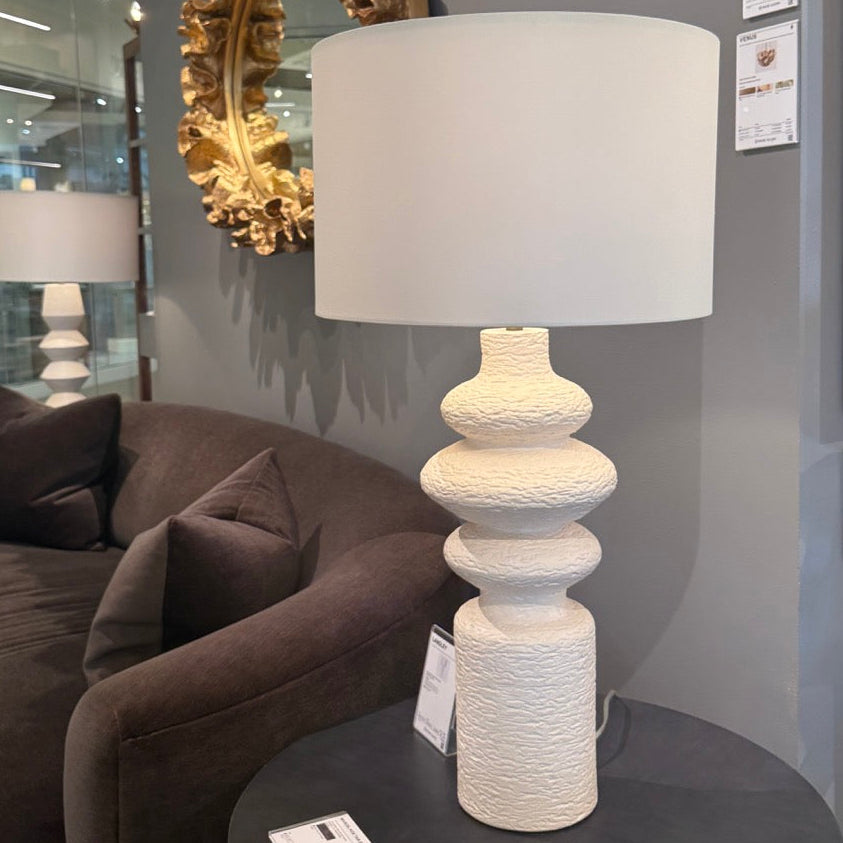 Decorative lamp with a textured base on a round table in a room setting.