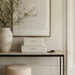 Three stacked rectangular storage boxes with textured cream shaker-style surfaces and small gold pull handles, displayed on a console table in a styled interior setting.