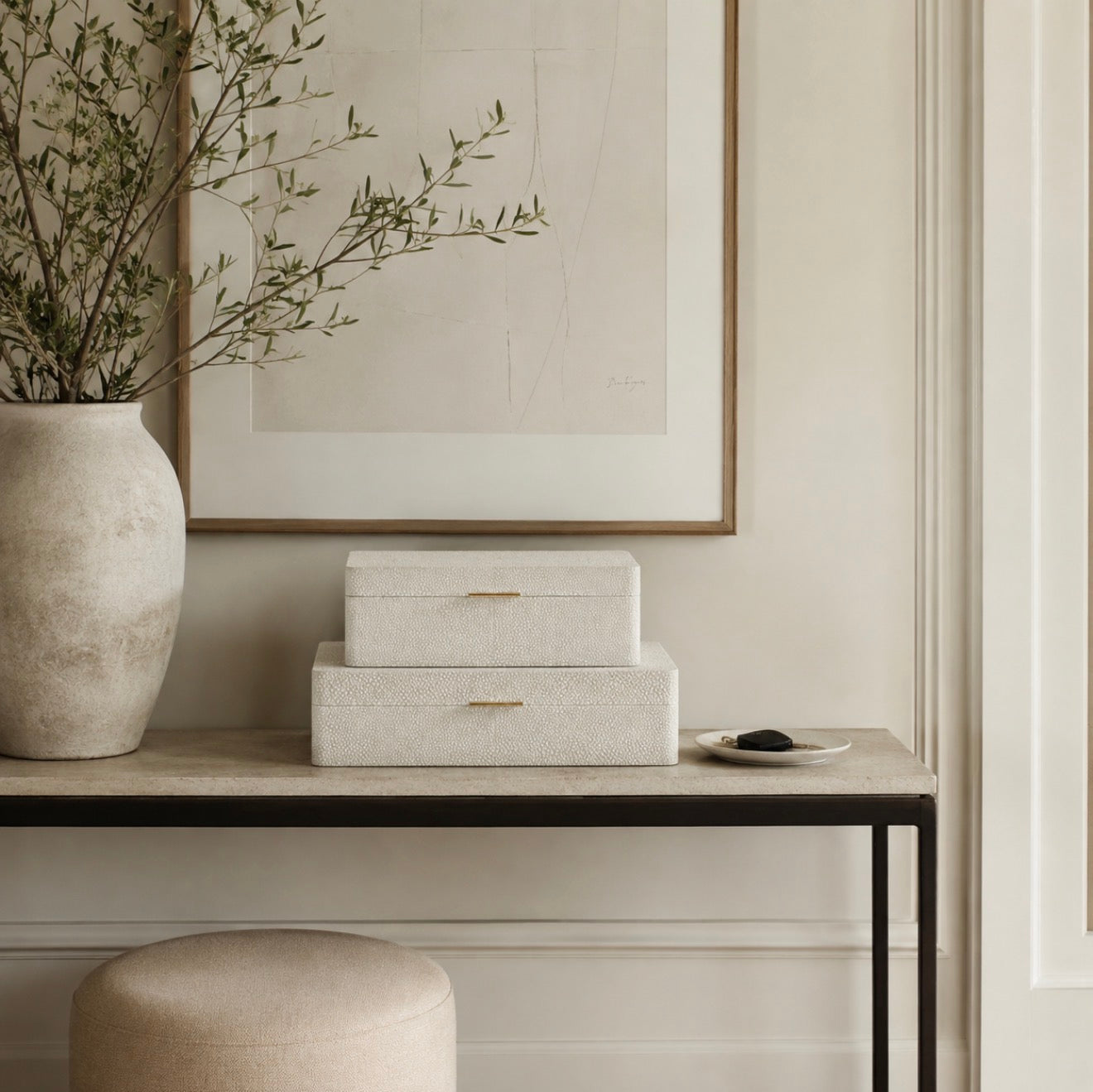 Three stacked rectangular storage boxes with textured cream shaker-style surfaces and small gold pull handles, displayed on a console table in a styled interior setting.