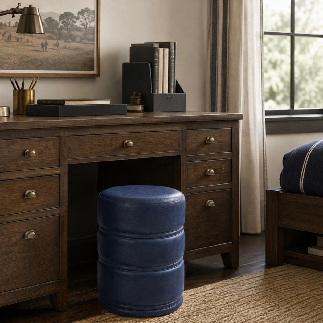 A dark brown wooden writing desk with brass hardware in a styled home office, featuring a cylindrical blue barrel stool in front of it.