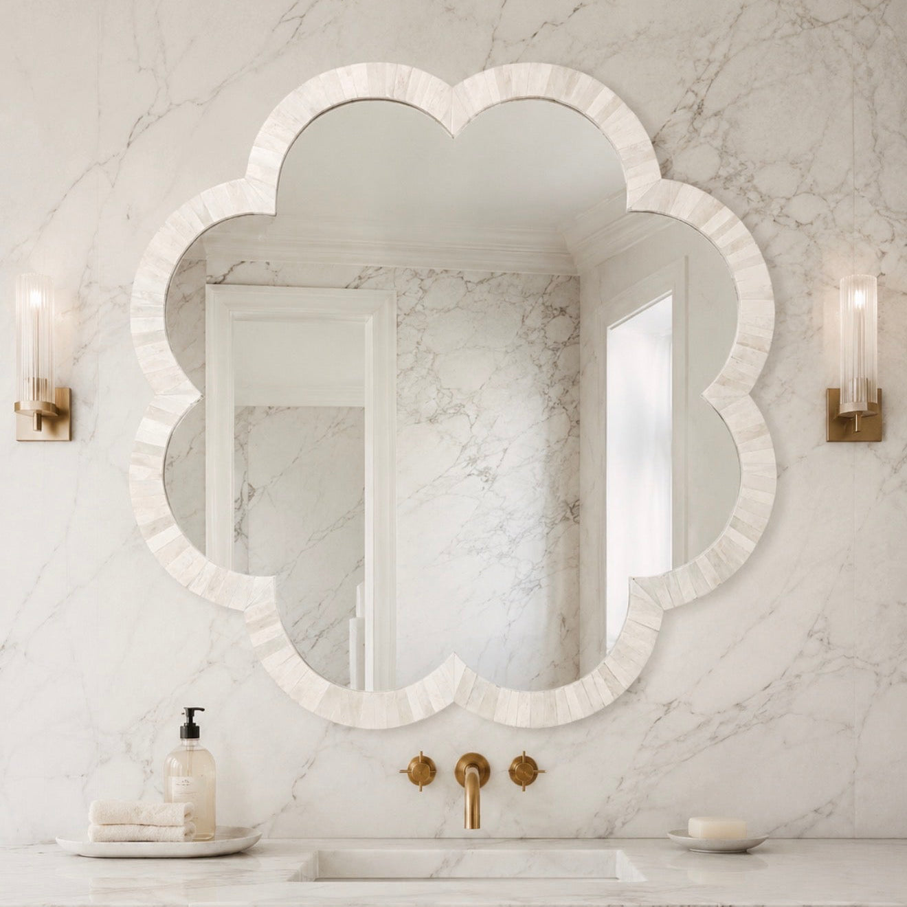 A scalloped white marble bathroom mirror with a tiered border, mounted on a white marble wall above a vanity with gold fixtures.