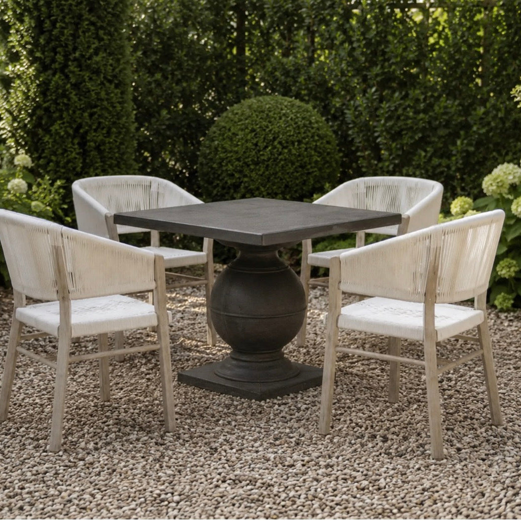 A 4-piece outdoor dining set featuring a square pedestal table and four matching armchairs with distressed off-white frames and white seats, set on a gravel patio in a garden.