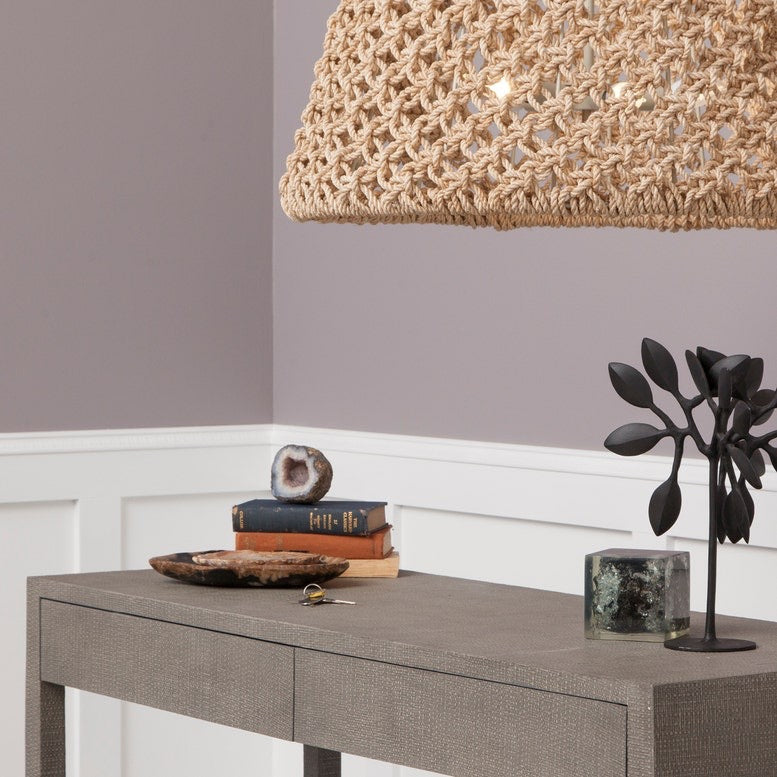 Gray console table with decorative items under a woven pendant light against a gray wall.