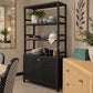 A tall black woven rattan hutch with five open shelves and two cabinet doors, styled in a dining room next to a wicker drawer cabinet.