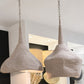 Two textured pendant light shades in a light beige woven fabric, suspended from silver chains in a modern interior setting.