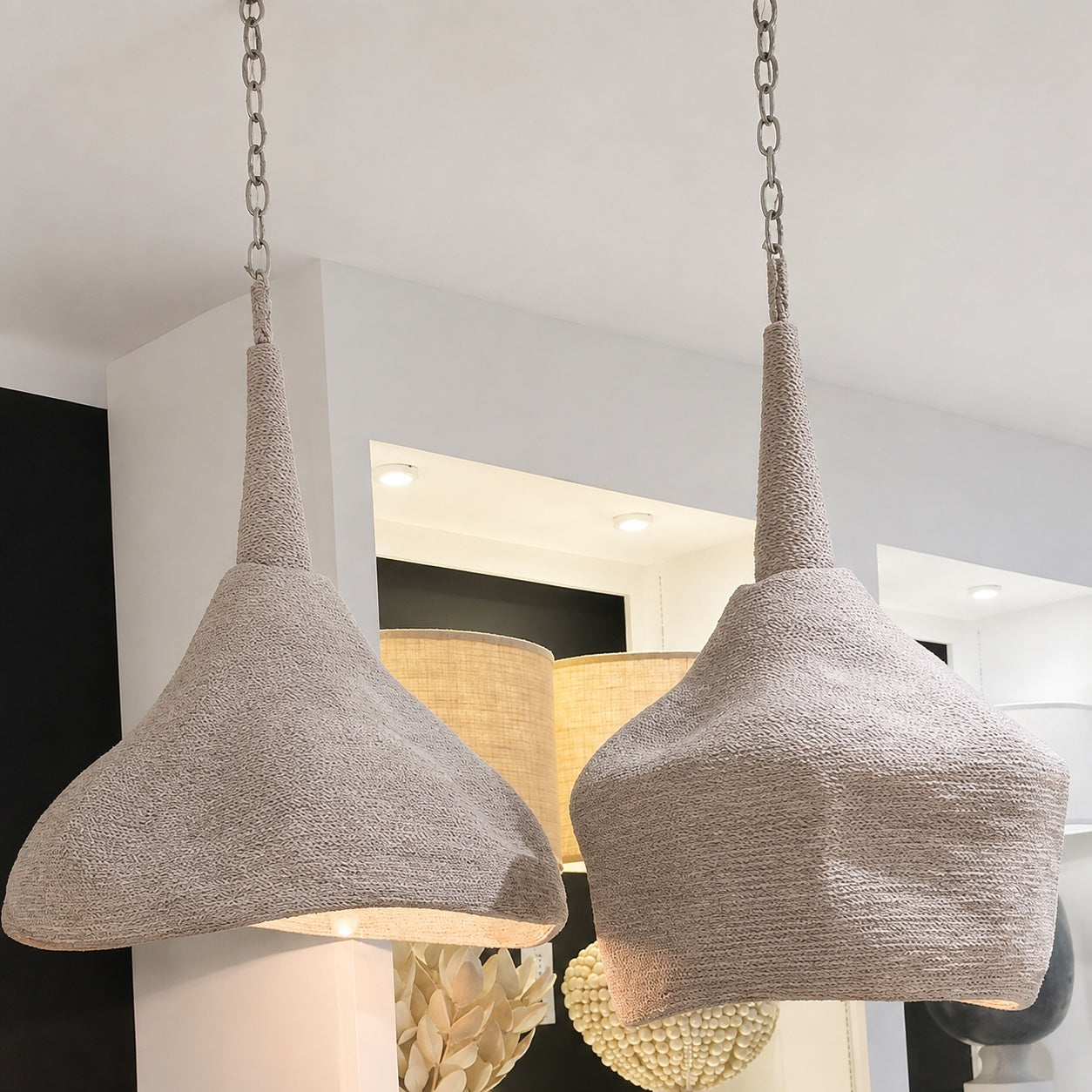 Two textured pendant light shades in a light beige woven fabric, suspended from silver chains in a modern interior setting.