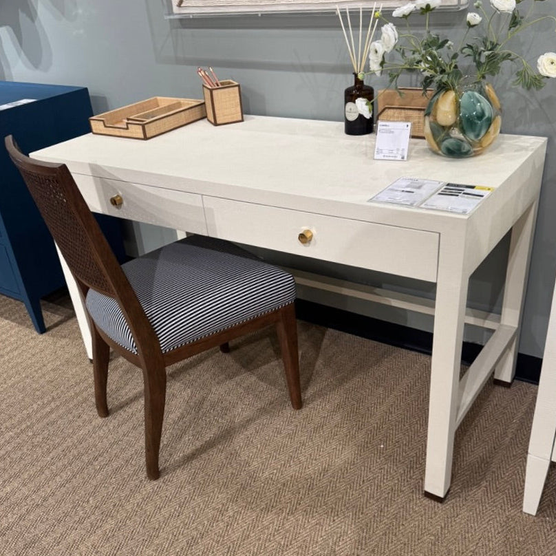 White desk with a chair in a room with a gray carpet and framed artwork on the wall.