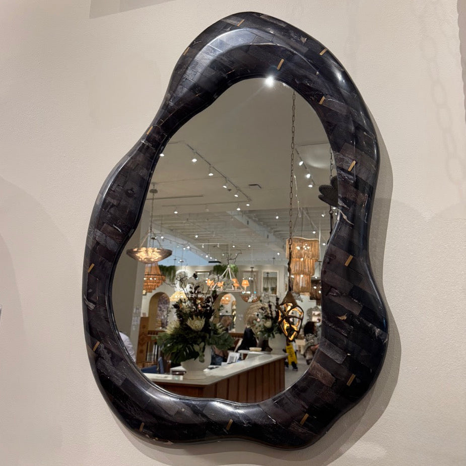 Black, wavy mirror on a wall with a blurred store interior in the reflection