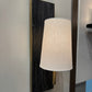 Wall-mounted lamp with a textured shade on a light-colored wall.