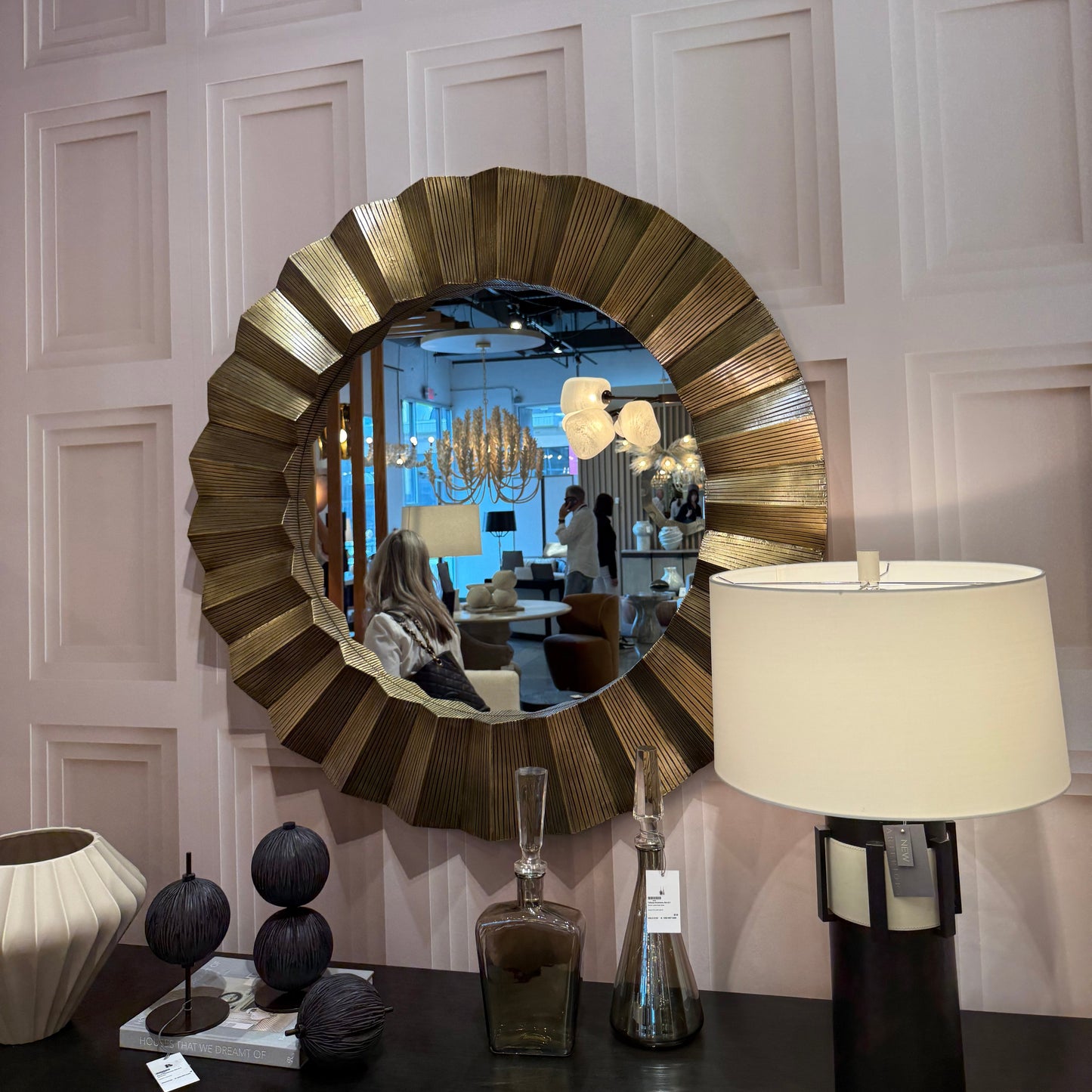 Round decorative mirror on a wall with a lamp and decor items below.
