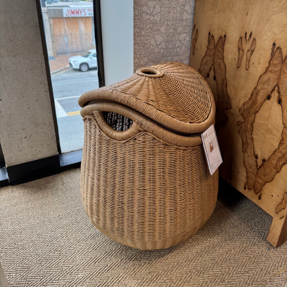 Wicker laundry basket with a lid on a carpeted floor next to a textured wall.
