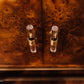 Close-up of two metallic cabinet handles mounted on a richly textured, swirling copper and gold burl wood door.