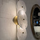 Modern wall sconce with glass shades and gold fixture on a textured wall.