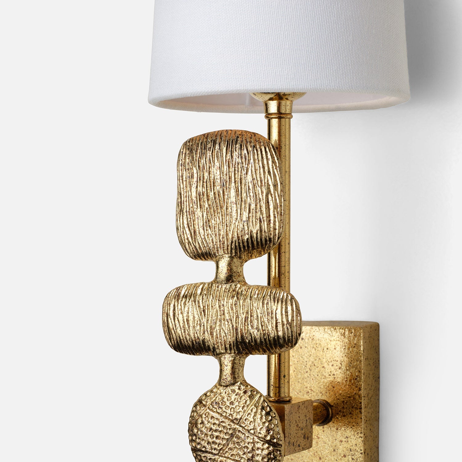 Decorative wall sconce with textured gold base and white shade on a light gray background