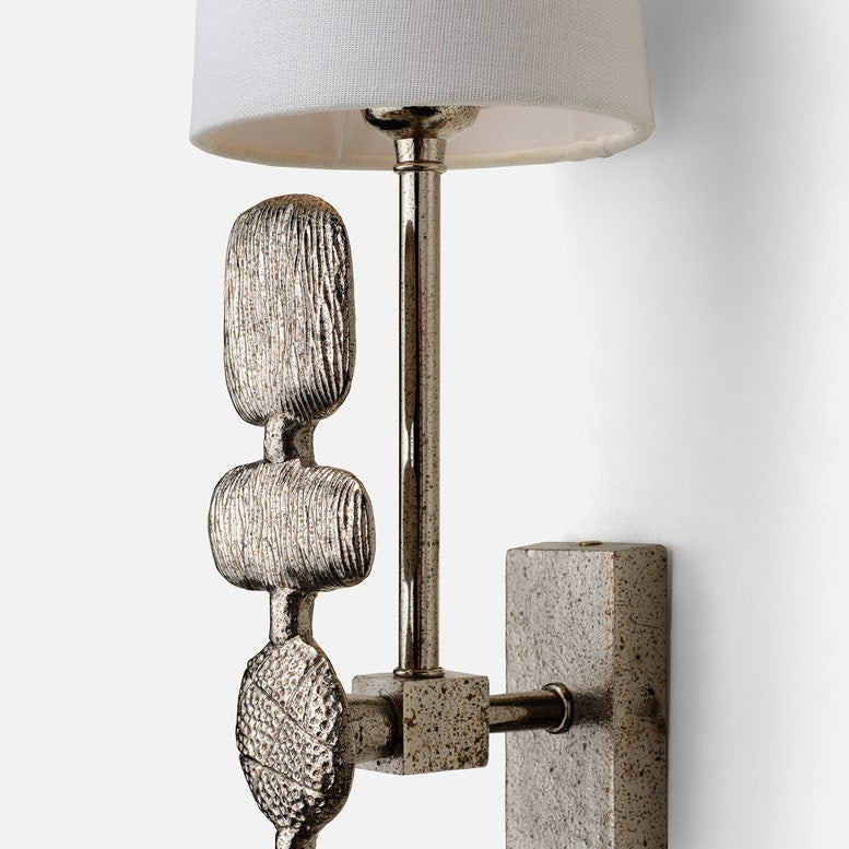 Decorative wall sconce with textured metal design and white lampshade on a light gray background