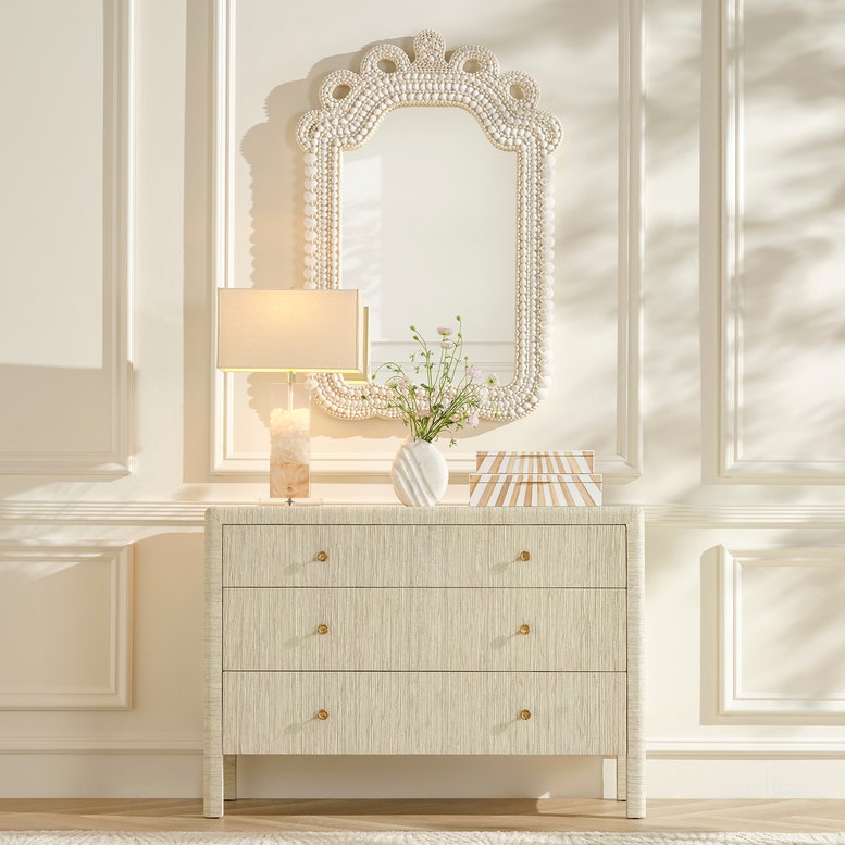 Decorative mirror above a dresser with a lamp and vase in a stylish room.