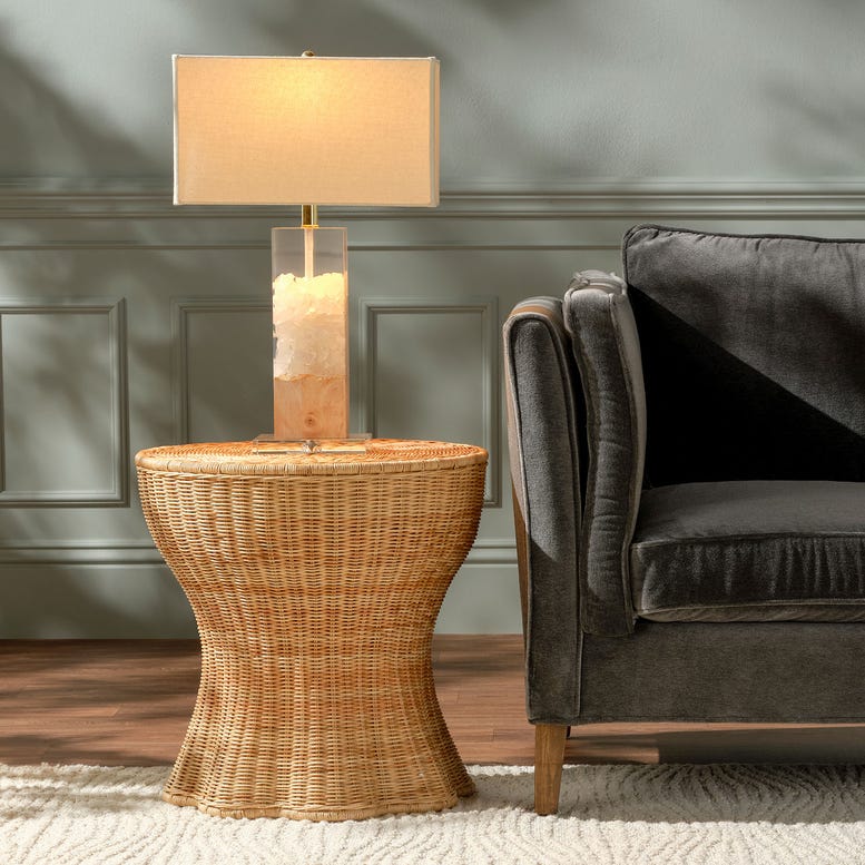 Wicker side table with a lamp next to a gray sofa against a gray wall.