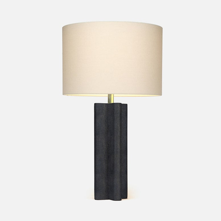 A modern table lamp with a dark charcoal gray sculptural base and a beige fabric drum shade, set against a plain light gray background.