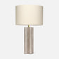 Textured neutral table lamp with a sculptural fluted base, brass accent, and large ivory drum shade on a white background.