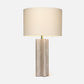 Textured neutral table lamp with a sculptural fluted base, brass accent, and large ivory drum shade on a white background.