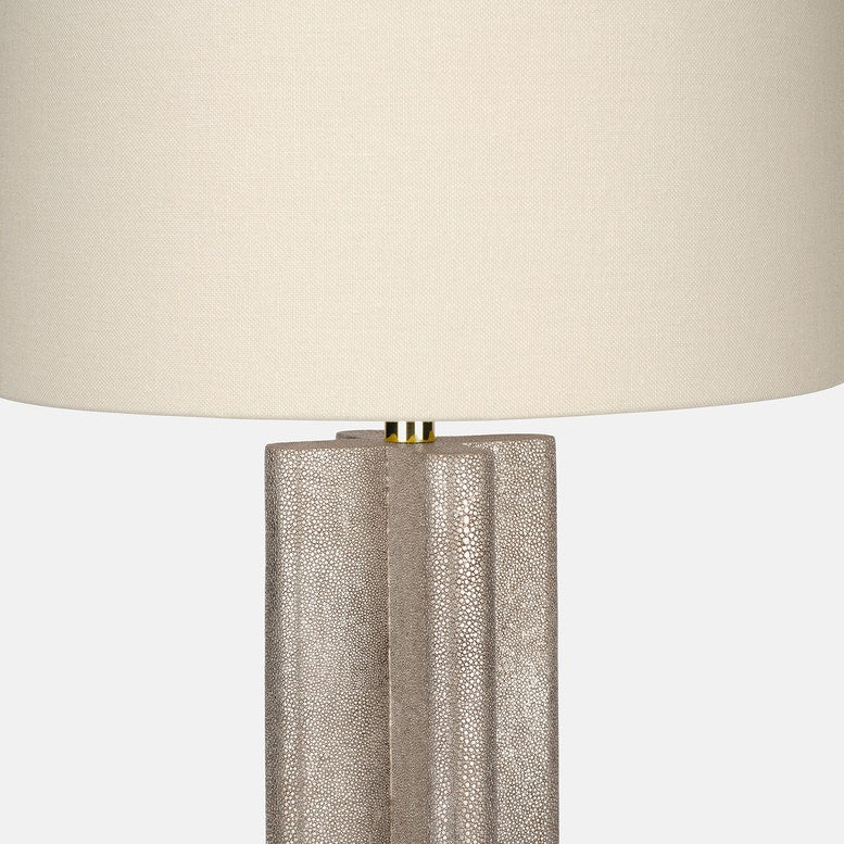 Textured neutral table lamp with a sculptural fluted base, brass accent, and large ivory drum shade on a white background.