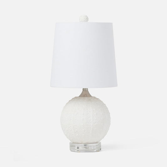 A table lamp with a textured white spherical base, a clear acrylic pedestal foot, and a white fabric drum shade topped with a small white pom-pom.