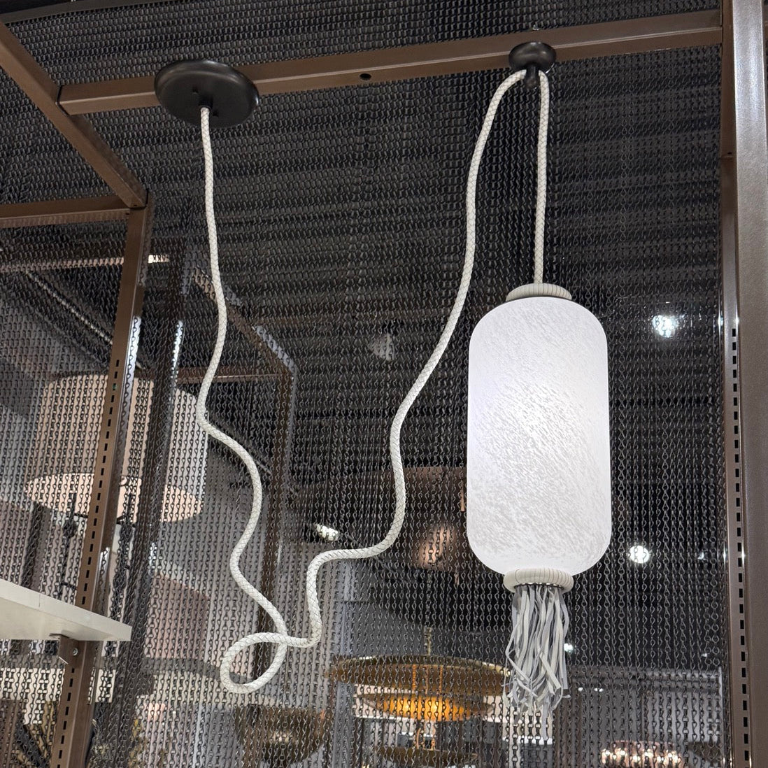 White textured pendant light hanging from a ceiling with a blurred indoor background