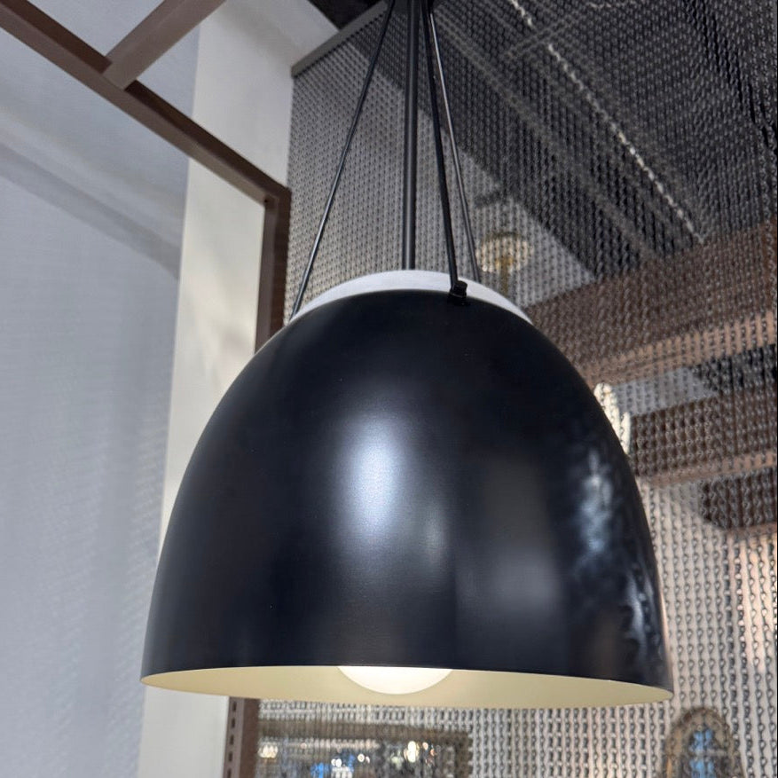 Black pendant light hanging in a modern interior setting with reflective walls.