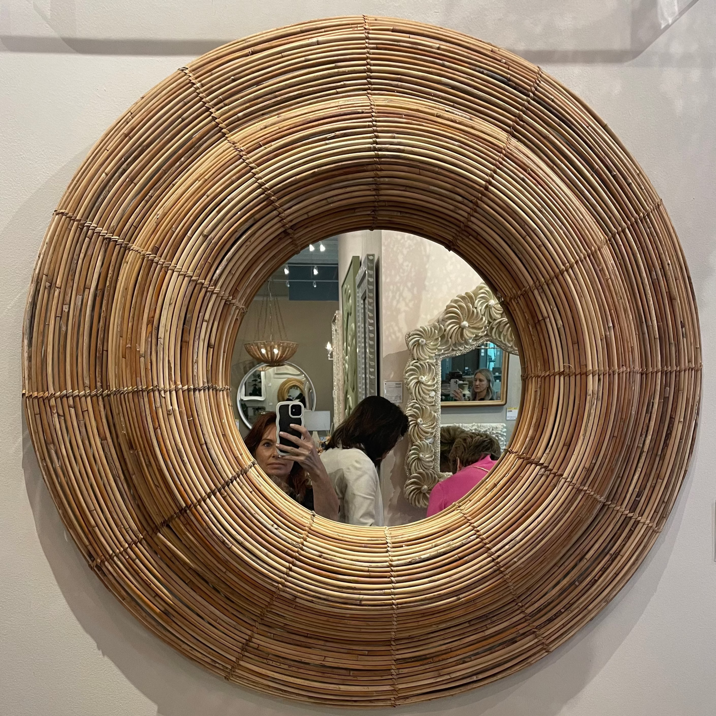Round woven mirror on a wall with a decorative shell on a table below.