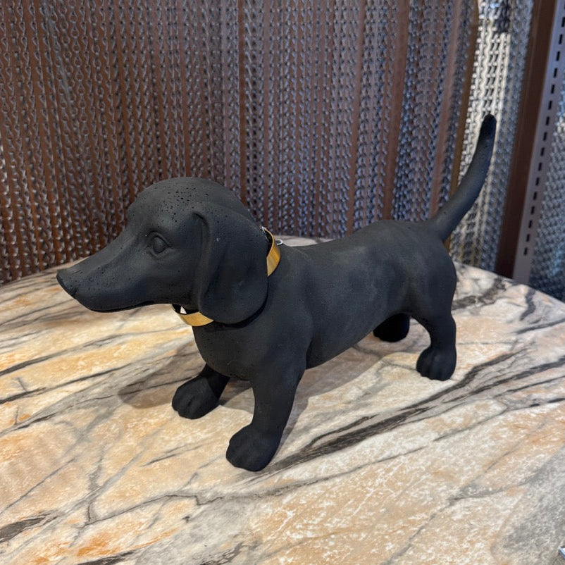 Black dog figurine on a stone surface with a metallic chain-link fence in the background