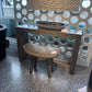 Small wooden stool with a round seat in front of a decorative wall with circular cutouts.