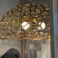 Decorative lamp with intricate design on a table next to a black sculpture and gray cushion.