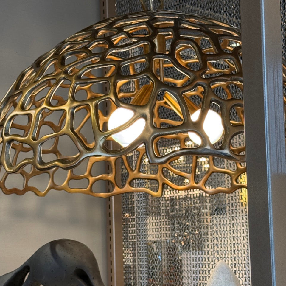 Decorative lamp with intricate design on a table next to a black sculpture and gray cushion.