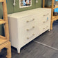 White dresser with gold handles in a room with wicker furniture and a mirror.