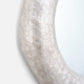A close-up of a curved mirror with a textured, organic shell-like frame in a pale ivory or off-white color, set against a clean white background.