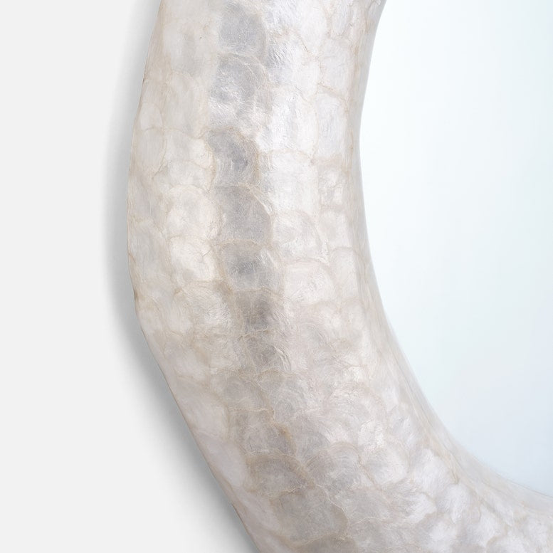 A close-up of a curved mirror with a textured, organic shell-like frame in a pale ivory or off-white color, set against a clean white background.
