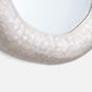 Close-up of a round wall mirror with a thick, textured off-white frame made of a stone-like material.