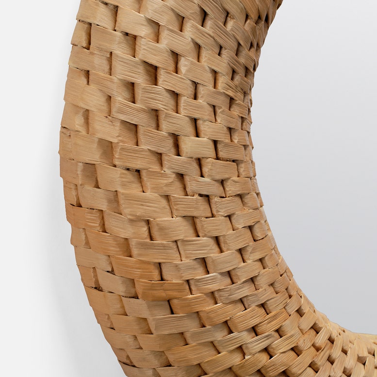Close-up of a woven natural fiber wall mirror frame, showing the detailed basketweave texture in warm tan and light brown tones against a light gray background.