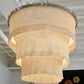 Chandelier with textured design hanging in a room with white ceiling panels.