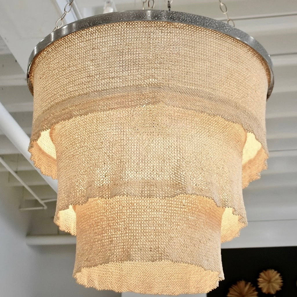 Chandelier with textured design hanging in a room with white ceiling panels.