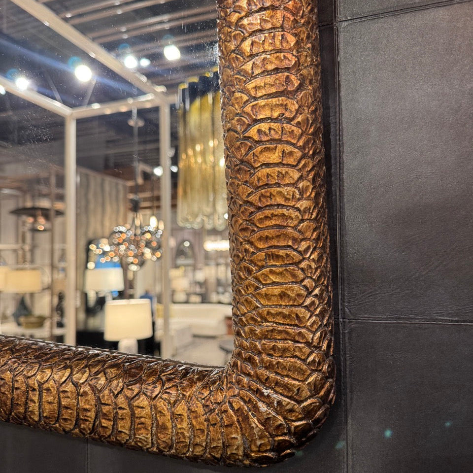 Decorative mirror with textured bronze frame on a dark wall.