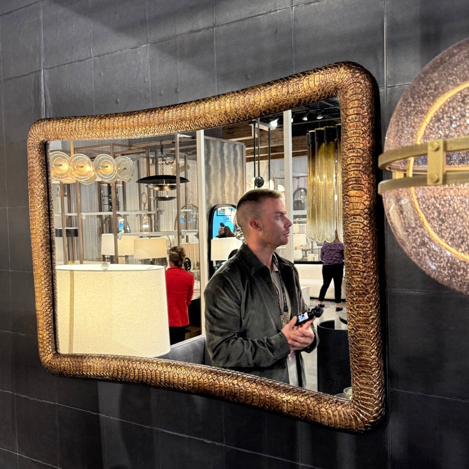 Man standing in a modern interior space with a decorative mirror and wall light fixture.