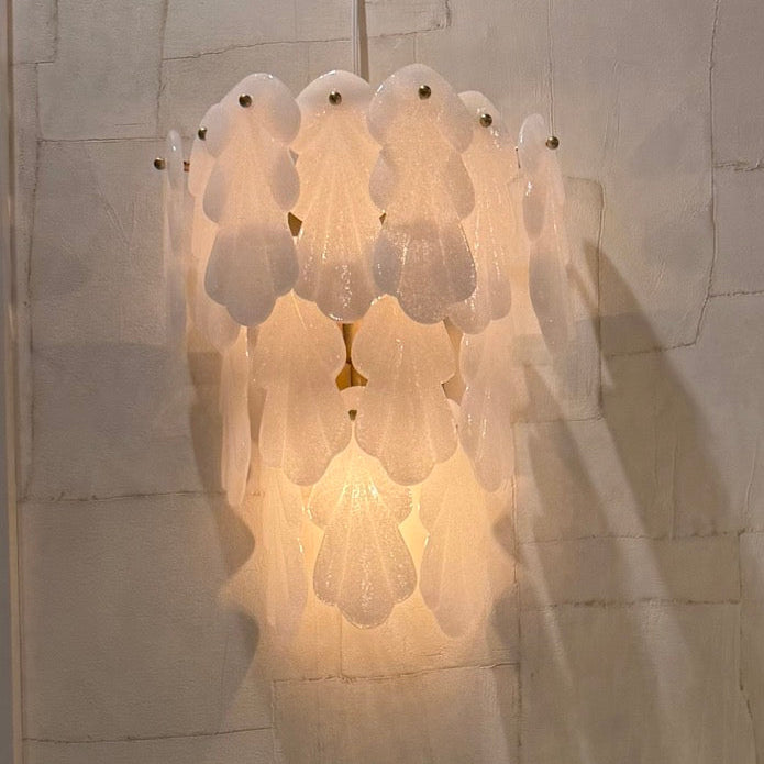 Wall-mounted light fixture with shell-like design on a textured wall.