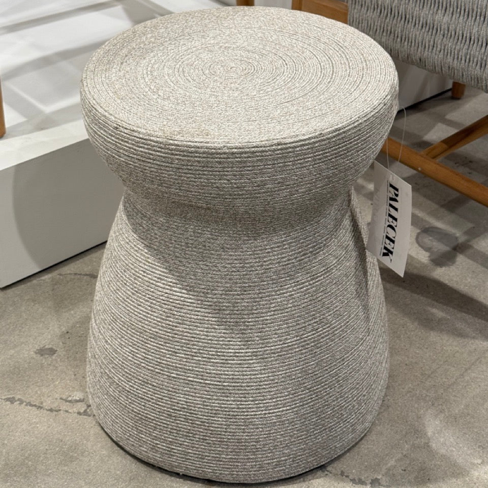Round woven stool on a floor with a chair and white bench in the background